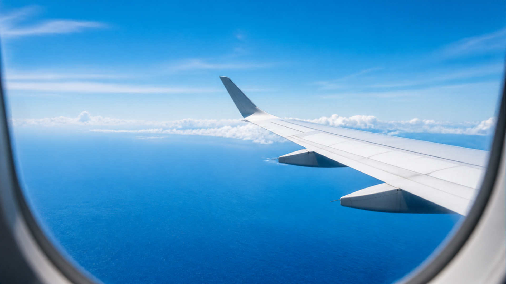 Aircraft wing over bright blue ocean through a cabin window