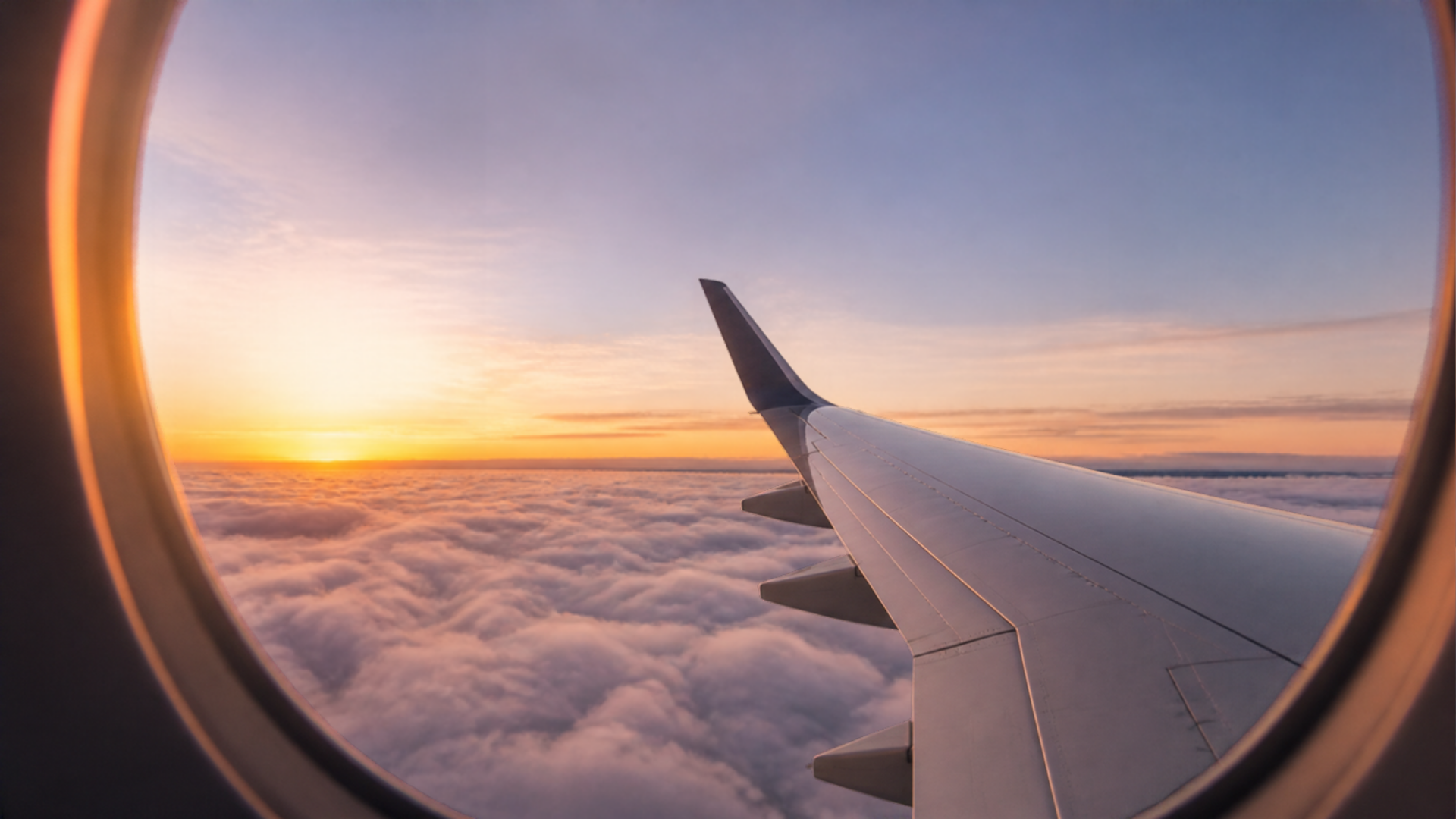 Aircraft wing over clouds at sunset through a cabin window