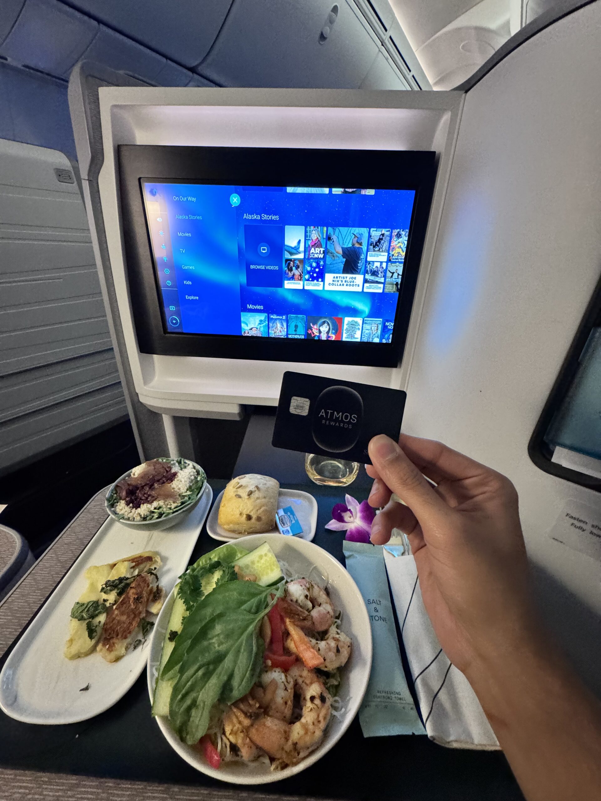Author holding the black Atmos Rewards card in an airplane cabin